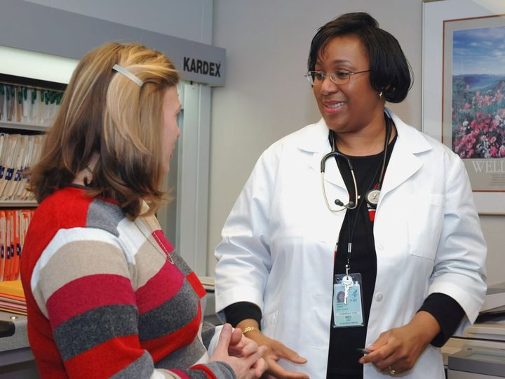 A clinician in a white coat talking with a woman in a consulting room