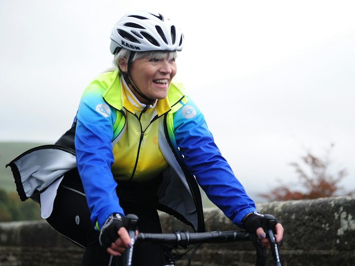 A woman smiling as she cycles over a stone bridge